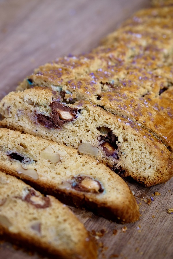 Slices of golden crunchy Italian biscotti baked with Whopper Malt Balls are lying side by side on walnut cutting board.


