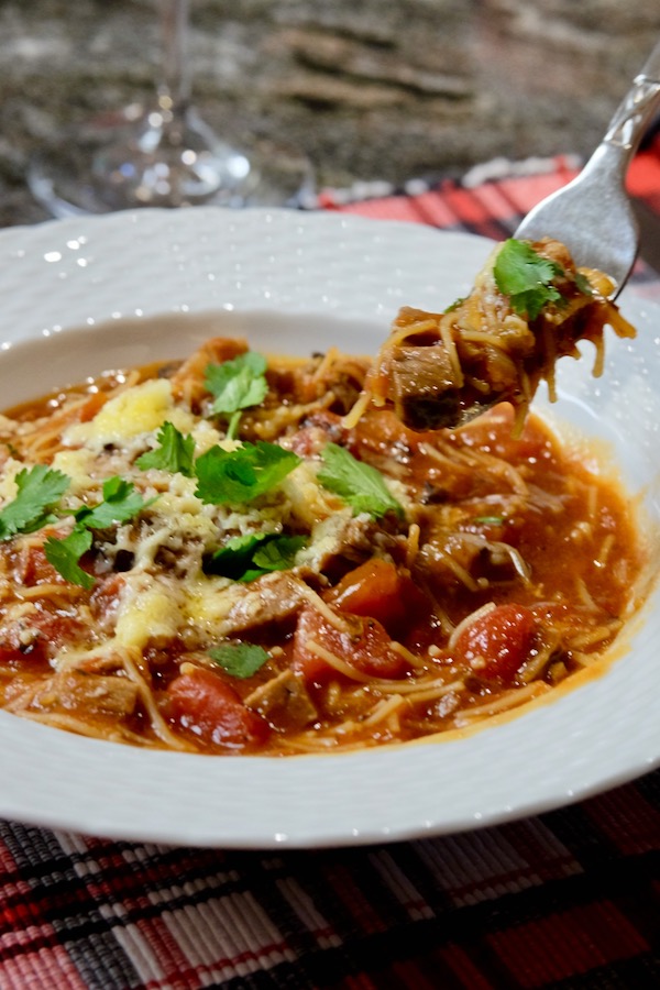 Sopa Seca de Fideo made with smoked brisket served in a white rimmed soup bowl with a fork full of noodle and meat hovering over the dish garnished with shredded cheese and cilantoro.