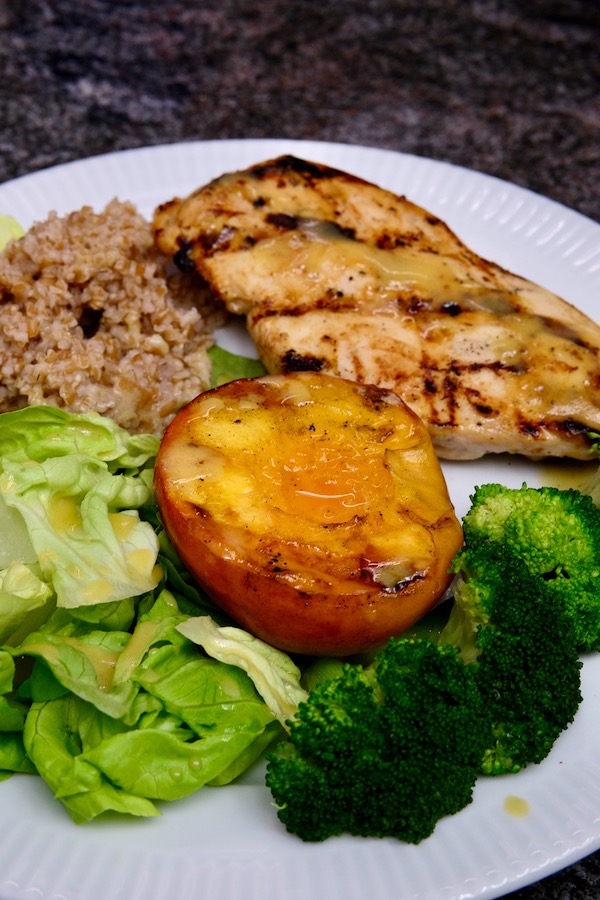 Grilled Peach is served front and center on a white plate next to Honey  Mustard grilled chicken flanked by steamed brocolli and bulgar salad. 