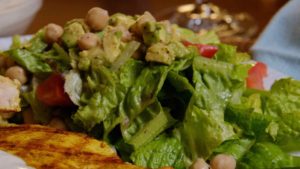 Green Mediterranean Salad with Lemon Sumac Dressing on white plate with grilled chicken in foreground.